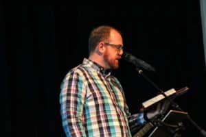 Man reading aloud from a book on a stage with a microphone at Howard Payne University. | HPU