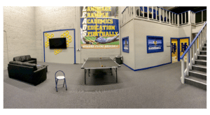 Recreational area with ping pong table, seating, and staircase, featuring Howard Payne University banners on the wall. | HPU
