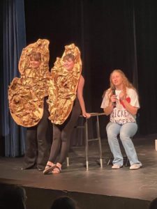 Two individuals dressed as peanuts stand next to a seated person holding a microphone on a stage at Howard Payne University. | HPU