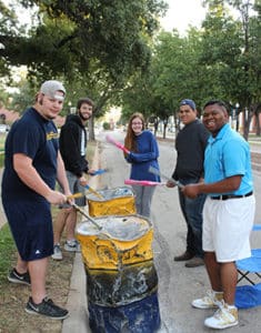 Group of Howard Payne University volunteers painting barrels outdoors. | HPU