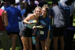 Two smiling young women enjoying an outdoor event at Howard Payne University with plates of food. | HPU