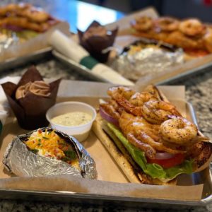 Assorted grilled foods including shrimp and a sandwich with a side of sauce and baked potatoes on a Howard Payne University kitchen counter. | HPU