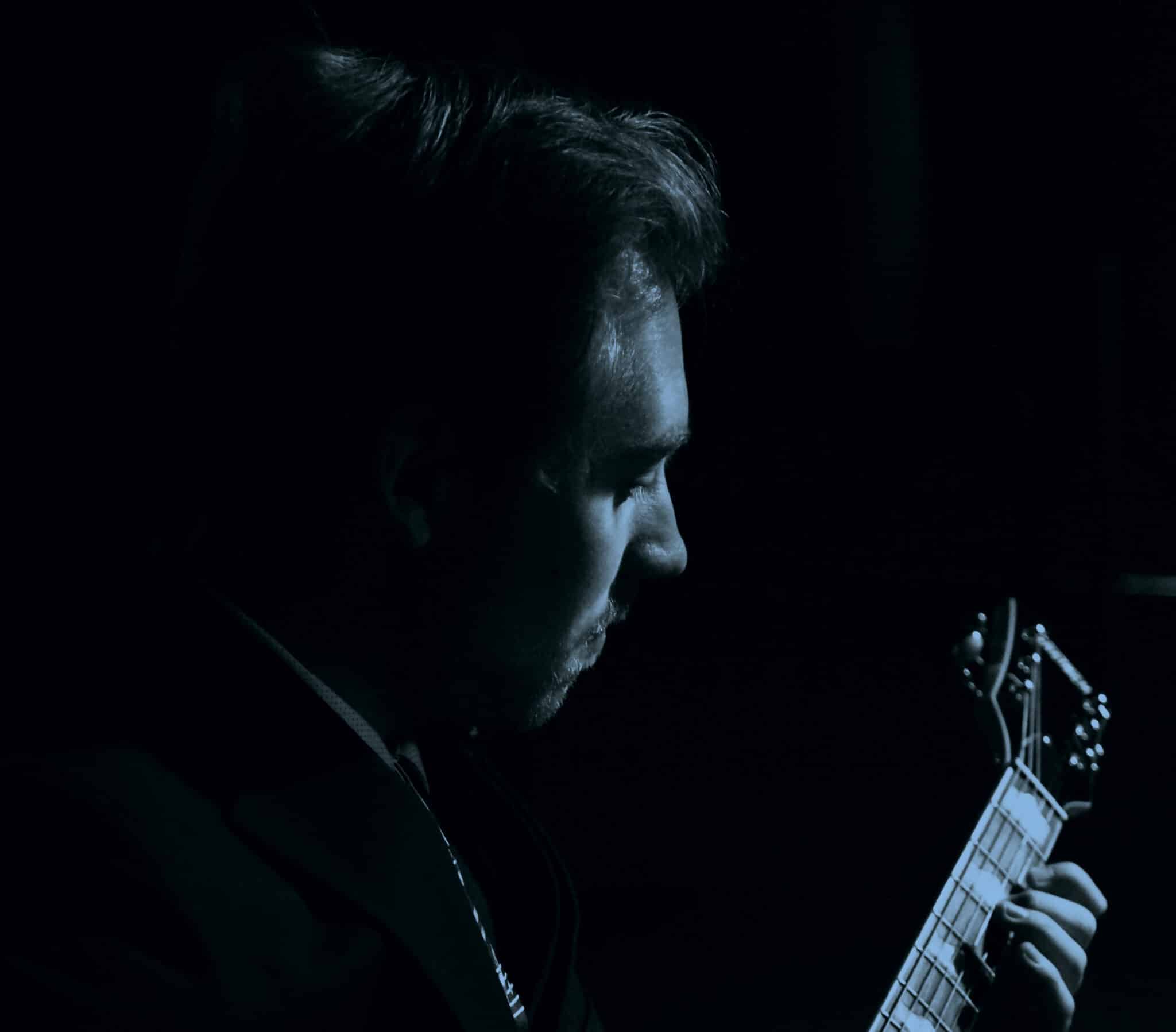 A musician from Howard Payne University playing guitar in low light. | HPU
