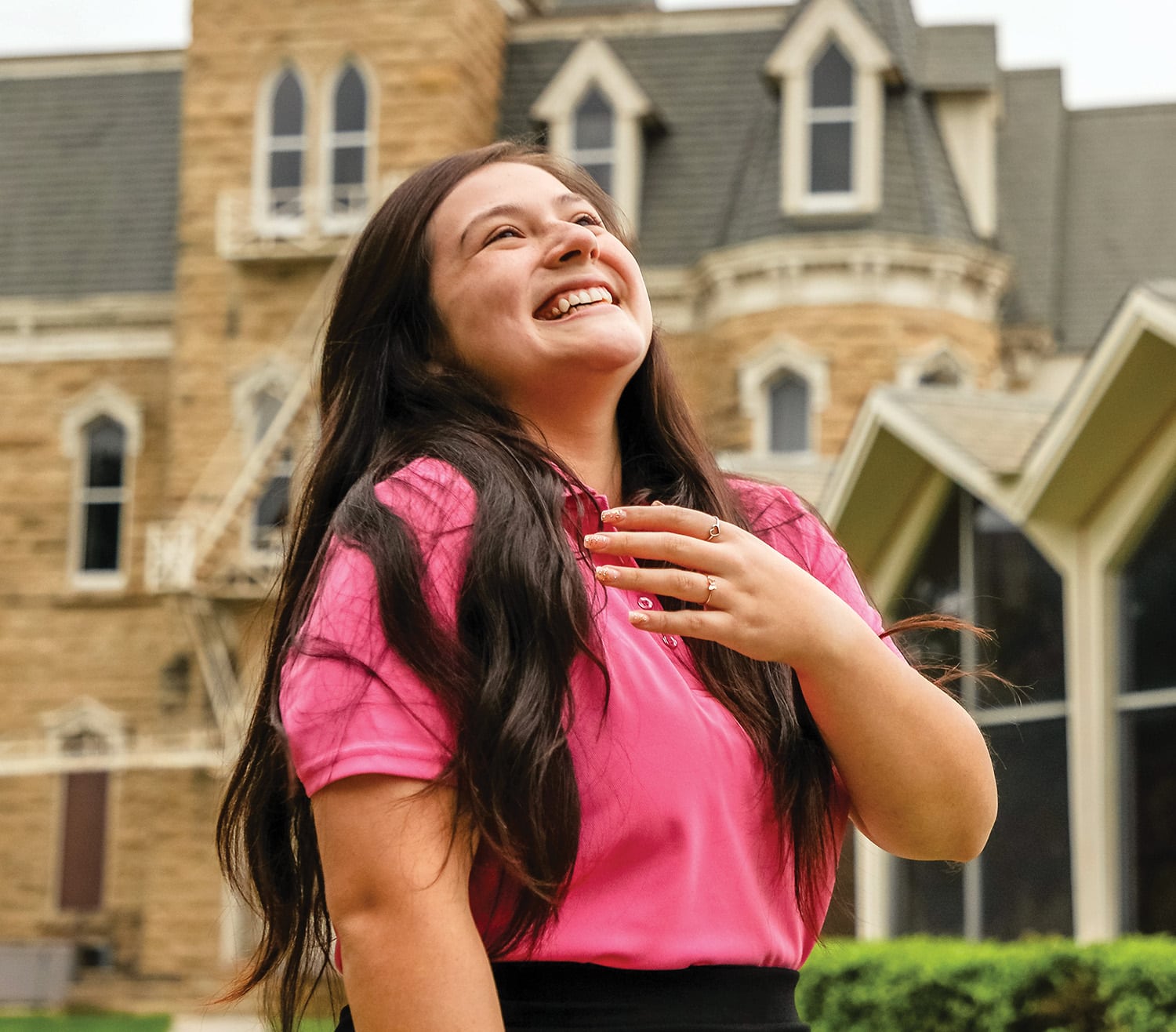 A joyful woman in a pink shirt laughing outdoors with Howard Payne University in the background. | HPU