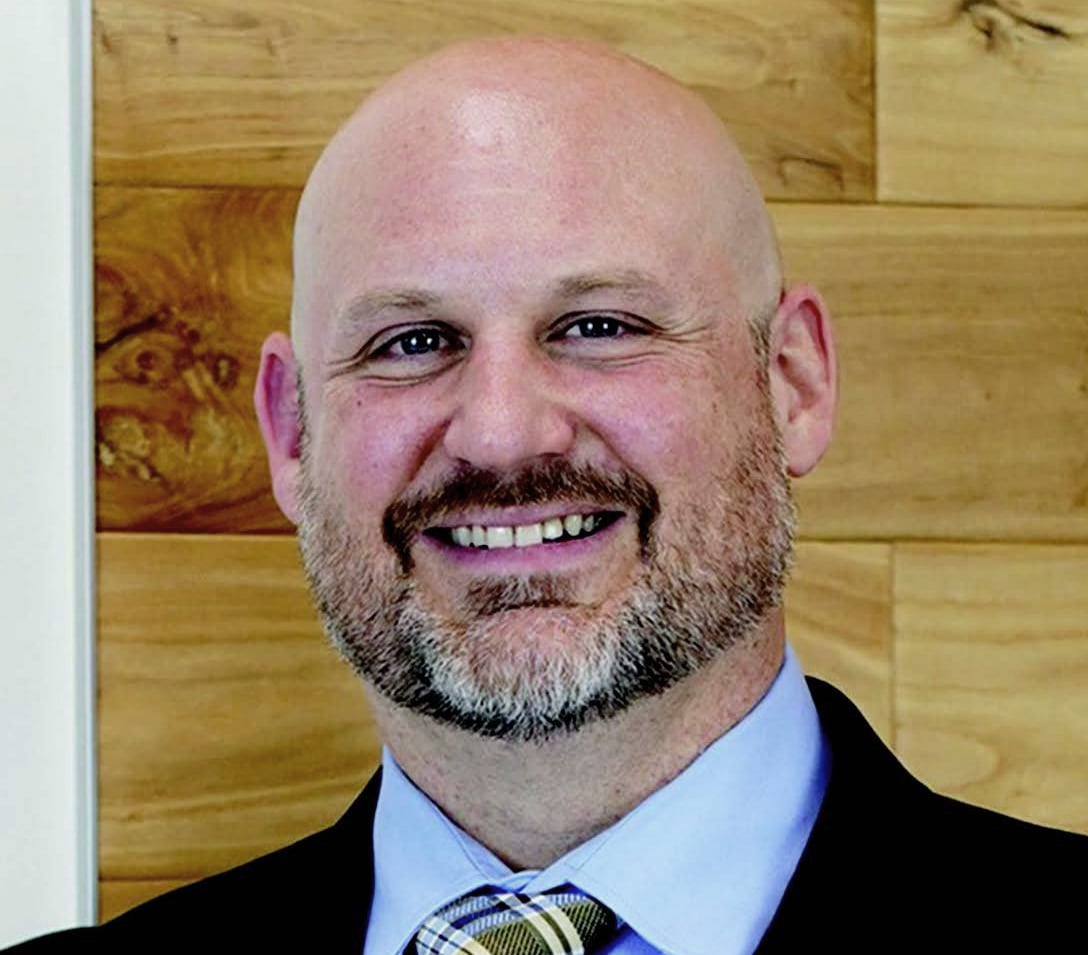 Bald man with a Howard Payne University beard smiling in front of a wooden background. | HPU