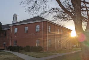 Sunset behind a brick building at Howard Payne University with trees in the foreground. | HPU
