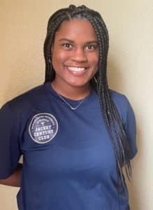 A smiling individual with braided hair wearing a Howard Payne University "jacket century club" t-shirt. | HPU
