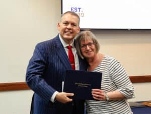 A man in a striped suit and a Howard Payne University woman stand close together, smiling and holding a certificate between them. | HPU