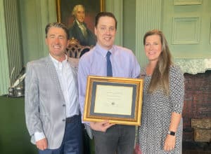 Three individuals posing for a photo at Howard Payne University, with the central person holding a framed certificate. | HPU