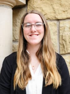 Smiling woman with glasses standing in front of a Howard Payne University stone wall. | HPU