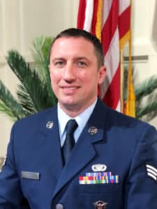 A man in a U.S. Air Force service dress uniform with medals stands in front of the American flag at Howard Payne University. | HPU