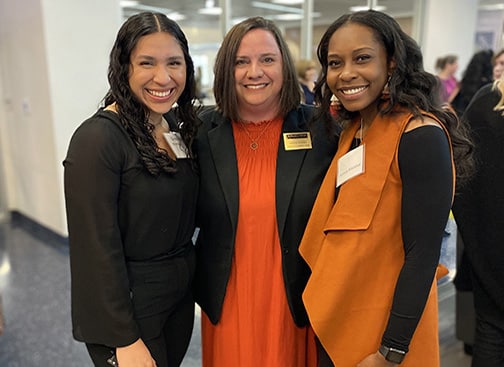 Three smiling women in professional attire with Howard Payne University name tags at an indoor event. | HPU
