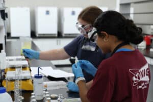 Summer Research Symposium participants Bethany Blair and Victoria Ramos work on their research in inhibiting bacterial growth.