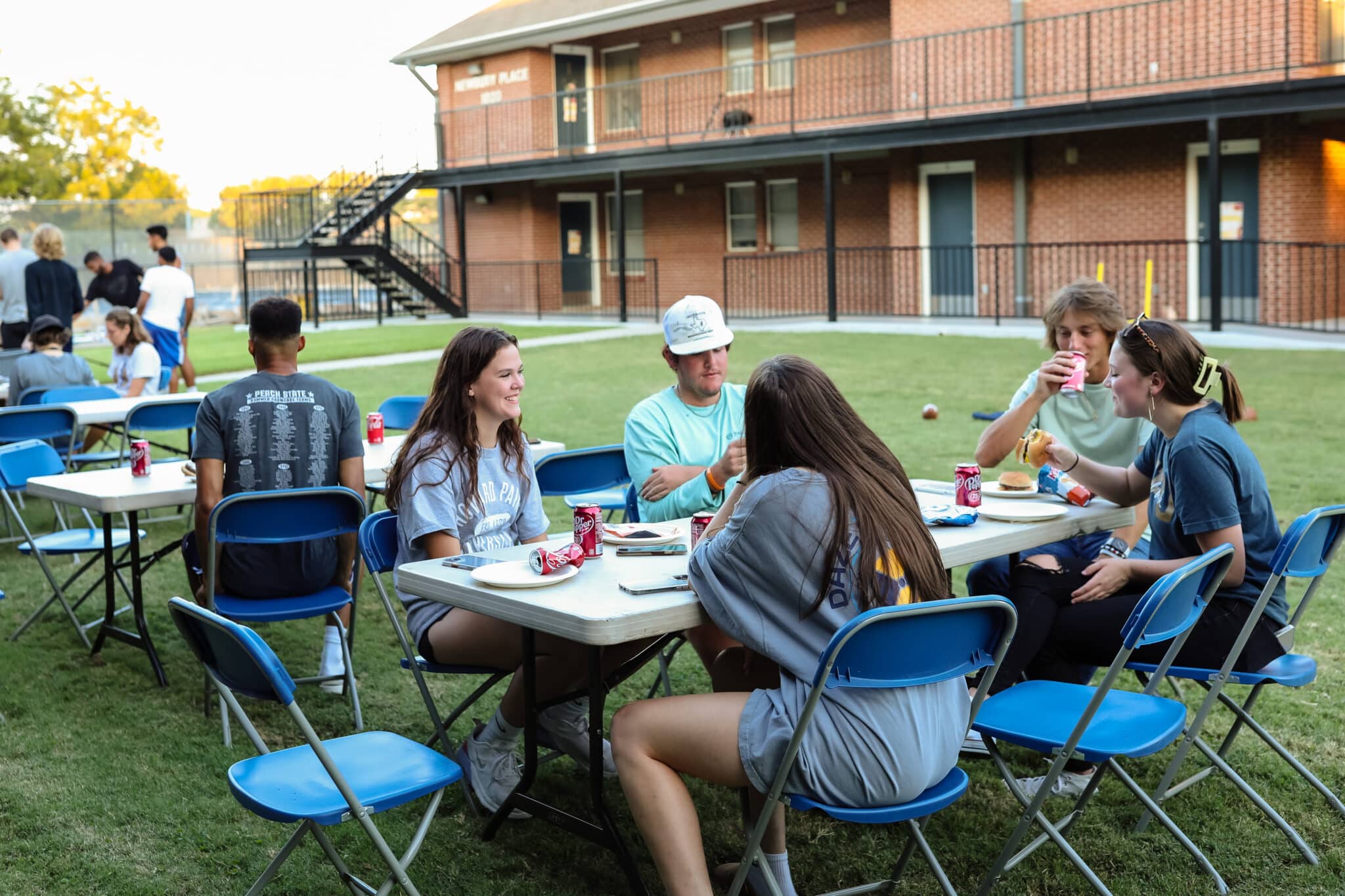 A group of students enjoy food together on the lawn between the Newbury Apartments