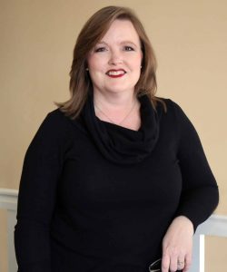 A woman in a Howard Payne University top poses with a slight smile against a beige background. | HPU