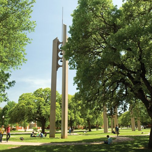 A Howard Payne University campus green space with students and a modern sculpture under a canopy of trees. | HPU