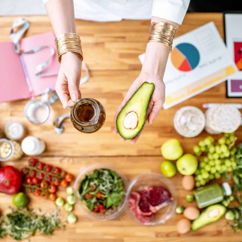 Dietitian holding avocado and olive oil above the table full of various healthy products, ketogenic diet concept